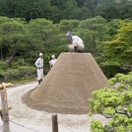 Ein Mann streicht einen Sandberg glatt und 3 andere halten die Leiter und geben Tipps